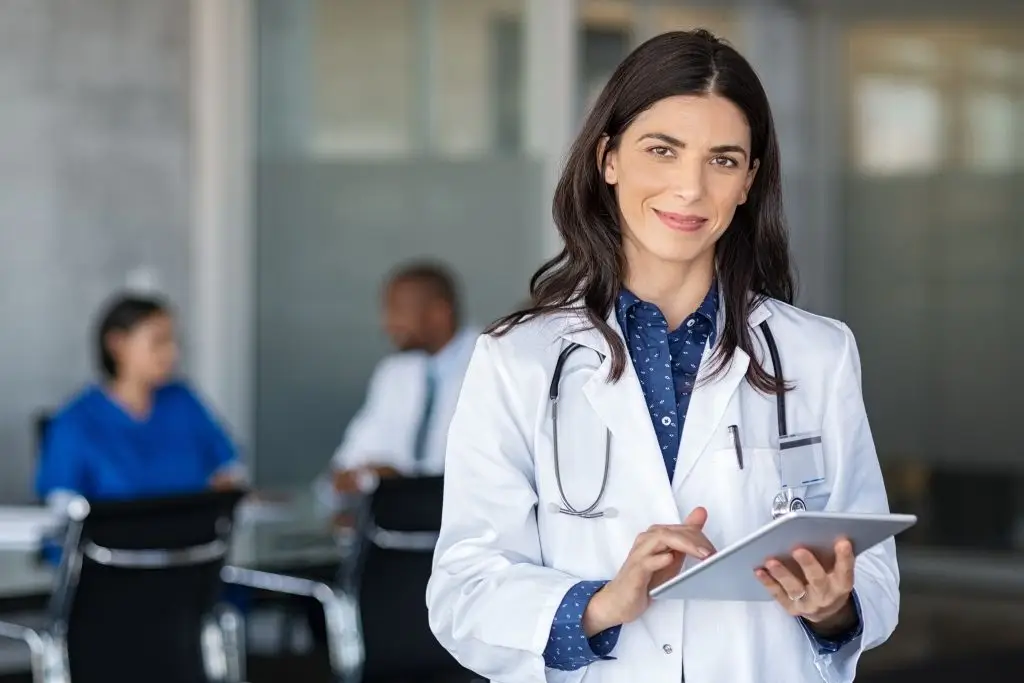 Un médecin en blouse blanche vérifie un comprimé et sourit.