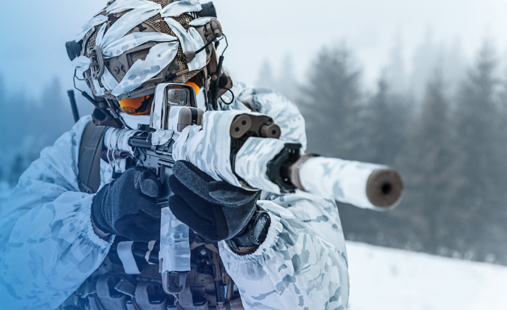 Un soldat en tenue de camouflage d'hiver vise un fusil à lunette dans une forêt enneigée.