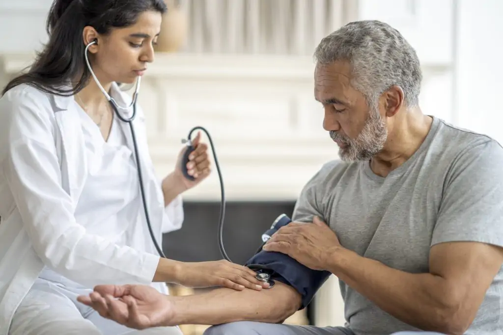 A healthcare professional measures an older man's blood pressure using a sphygmomanometer and stethoscope.