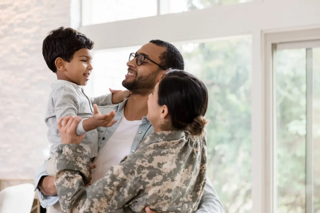 A man and woman in uniform are holding their son in their living room.