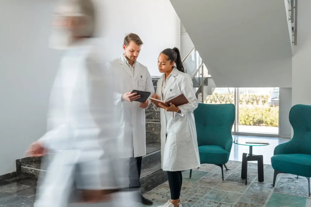 Two doctors in white coats standing in a lobby while doing research.