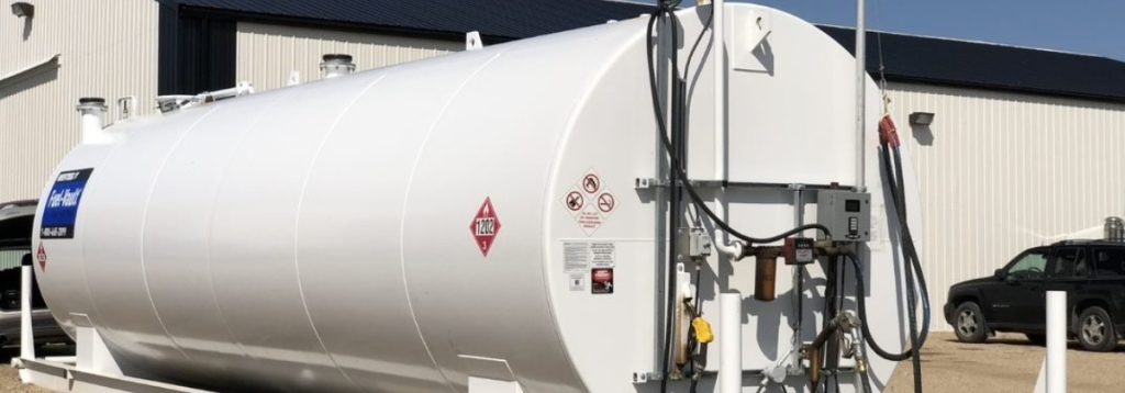 A horizontal white fuel storage tank with warning labels and a metering pump station outdoors.