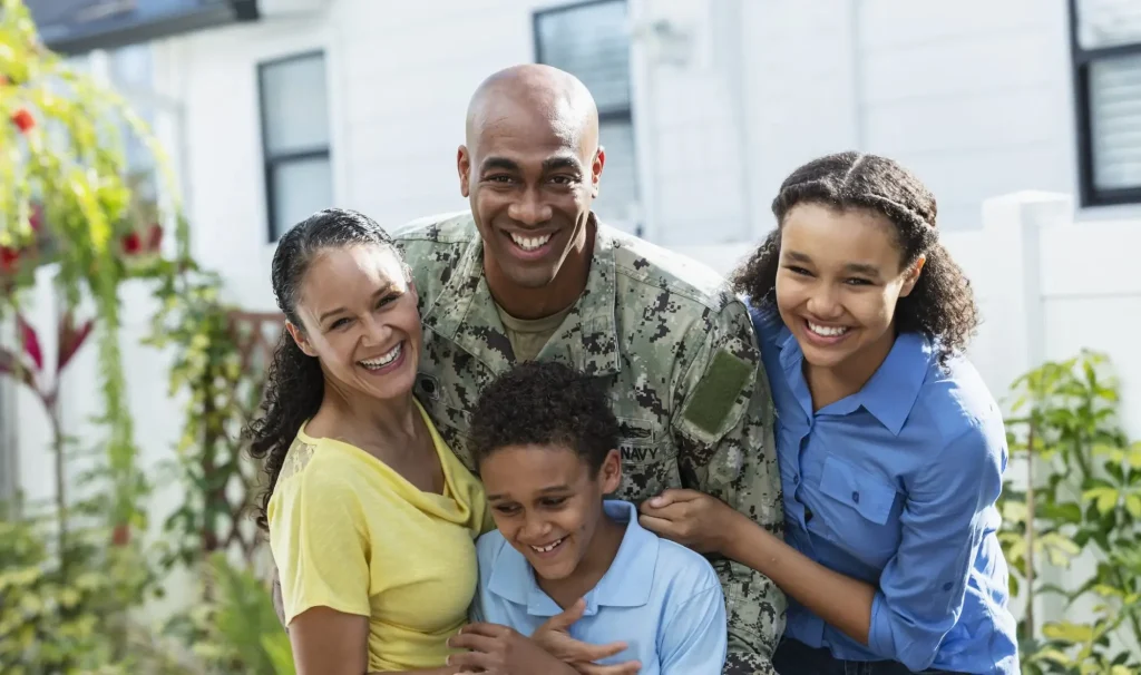 A military family posing for a photo in front of their home.