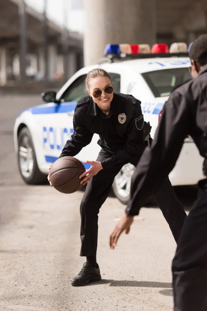 Two police officers playing basketball in front of a police car.