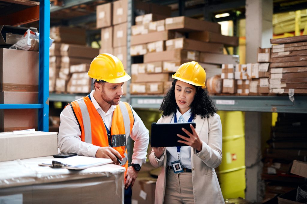 A man and woman wearing hard hats looking at a tablet.