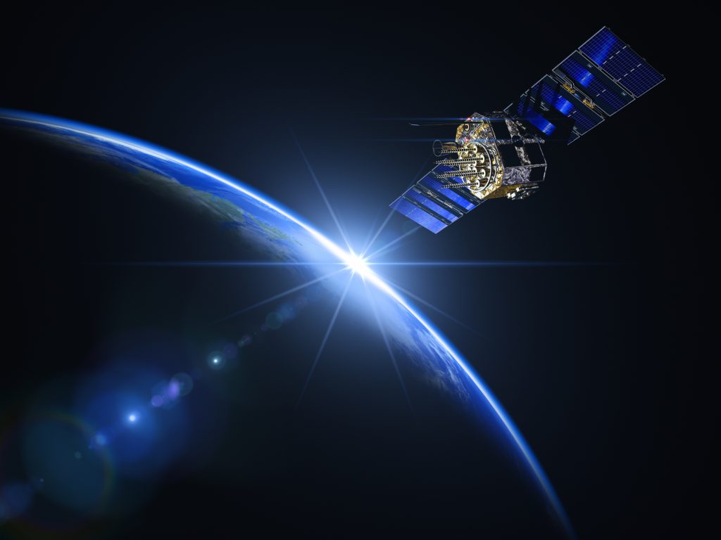 Un satellite est en orbite au-dessus de la Terre, le soleil étant visible à l'arrière-plan et éclairant l'atmosphère de la planète.