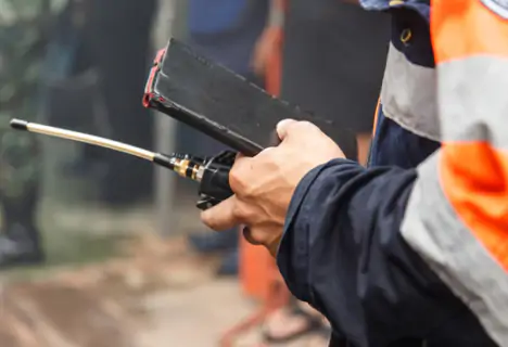Person in a uniform holding a walkie-talkie and a notepad, with other people blurred in the background.