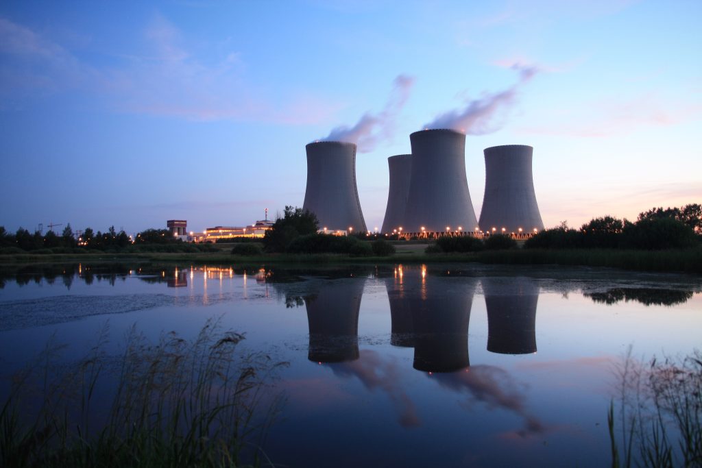 Les tours de refroidissement d'une centrale nucléaire rejettent de la vapeur au crépuscule, leur reflet se dessinant sur une étendue d'eau calme au premier plan.