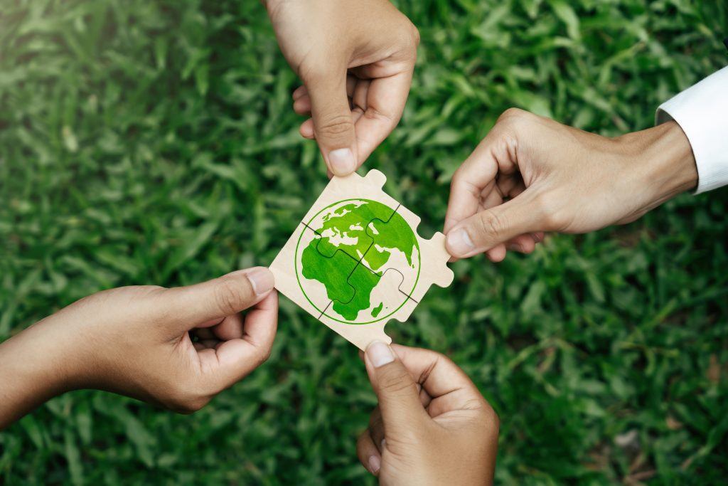 Quatre mains tiennent des pièces d'un puzzle représentant une Terre verte, qu'elles assemblent sur un fond d'herbe verte.