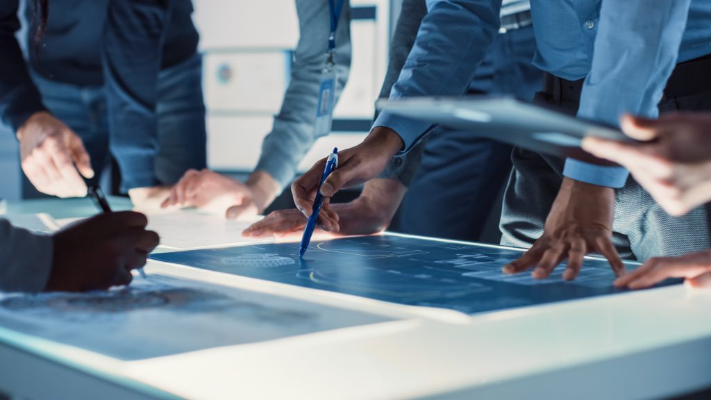 Un groupe de professionnels, dans un bureau, examine des plans techniques affichés sur une table lumineuse.